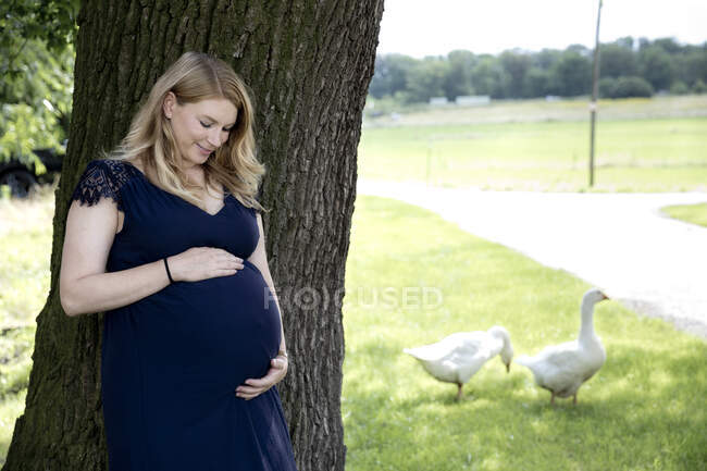 Smiling pregnant woman standing by tree trunk — Stock Photo