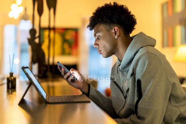 Giovane uomo che utilizza smart phone dal computer portatile sul tavolo a casa — Foto stock