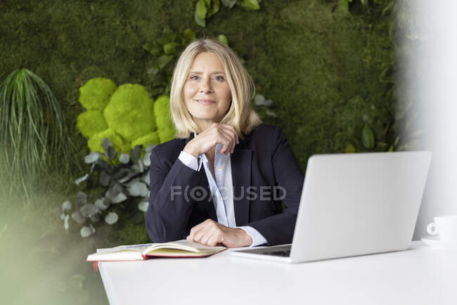 Красивая блондинка бизнес-леди в черной куртке с ноутбуком в офисе | Премиум Фото