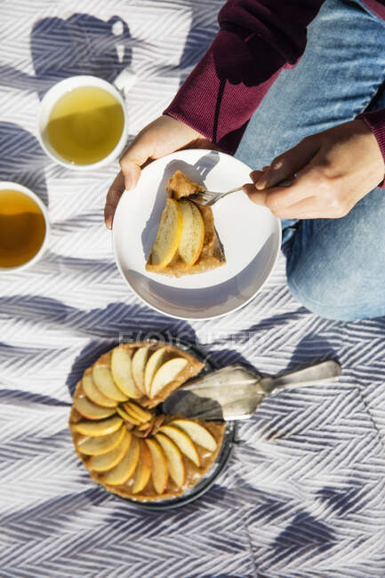 Mani di donna che mangia torta di mele appena sfornata sulla coperta da picnic — Foto stock