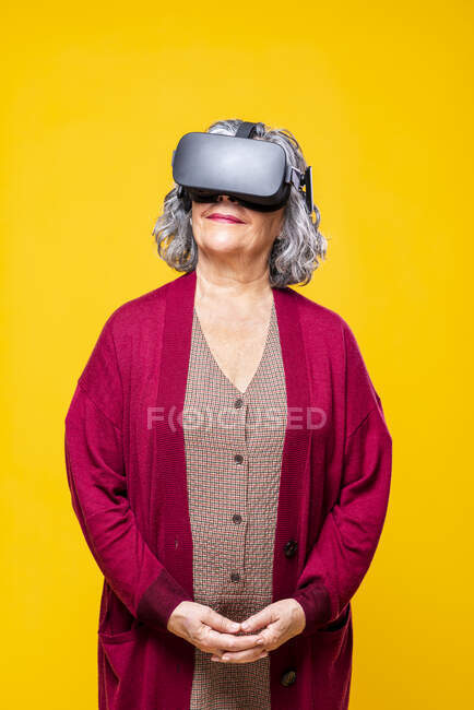 Улыбающаяся пожилая женщина с гарнитурой виртуальной реальности на жёлтом фоне — стоковое фото