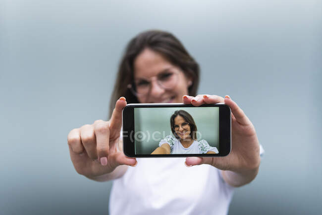 Улыбающаяся молодая женщина фотографирует через смартфон — стоковое фото