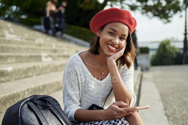 Mulher sorridente com a mão no queixo segurando telefone celular por mochila — Fotografia de Stock