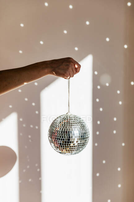 Young woman holding shiny disco ball in front of wall at home — Stock Photo