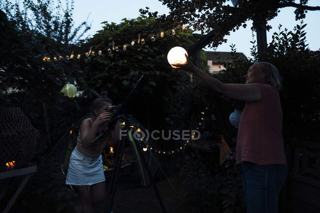 Ragazza guardando lanterna illuminata tenuto da donna anziana attraverso il telescopio — Foto stock