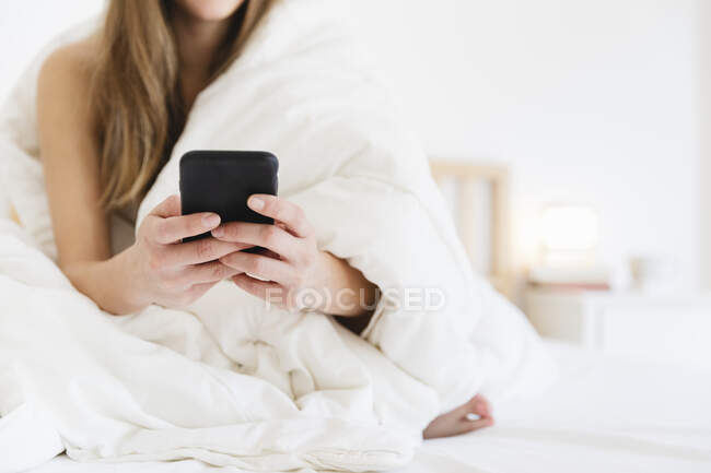 Young woman using mobile phone while sitting on bed in bedroom — Stock Photo