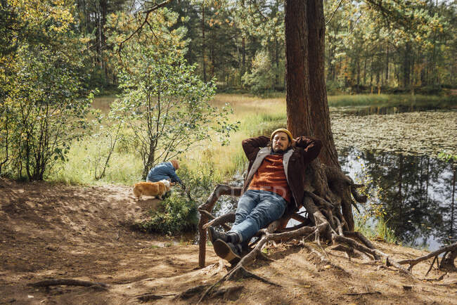 Homme avec les mains derrière la tête relaxant par l'arbre dans la forêt — Photo de stock