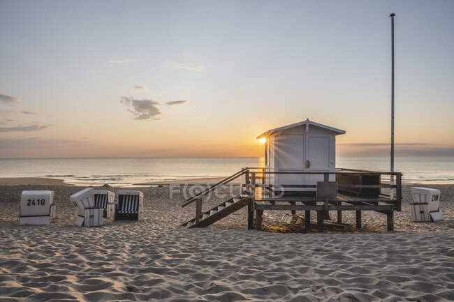 Lifeguard hut and hooded beach chairs at sandy coastal beach during sunset — Stock Photo
