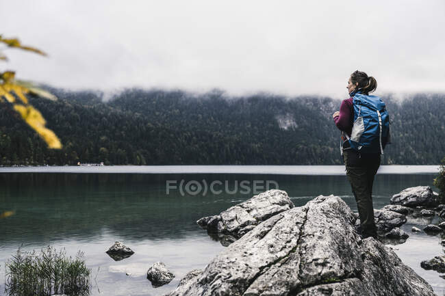 Mochilero hembra de pie en la roca junto al lago - foto de stock