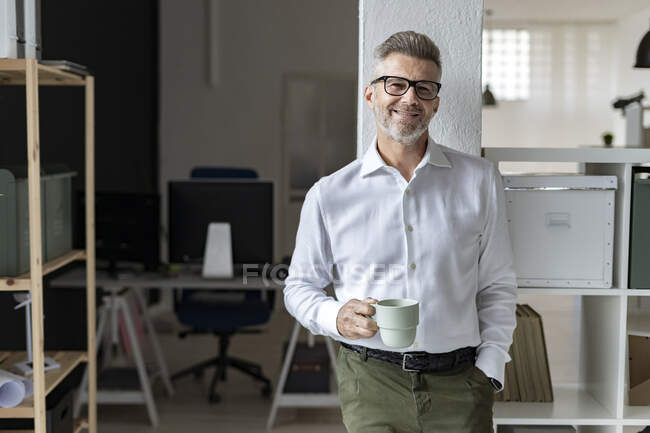 Homme d'affaires souriant avec tasse à café appuyé sur la colonne architecturale — Photo de stock