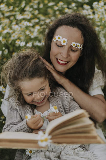 Alegre madre e hija con flores y libro en el campo agrícola - foto de stock