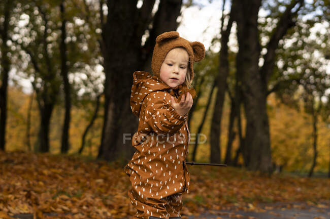Fille portant imperméable tenant feuille dans le parc d'automne — Photo de stock