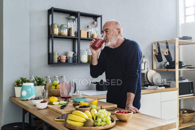 Чоловік п'є коктейль, стоячи на кухні. — стокове фото