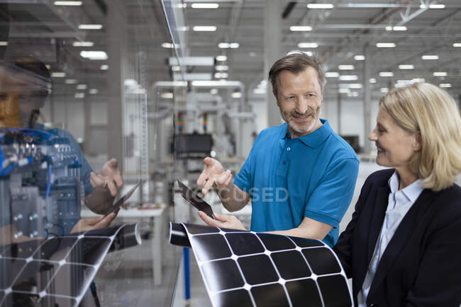 Smiling male and female professionals discussing over solar panel in factory — Stock Photo