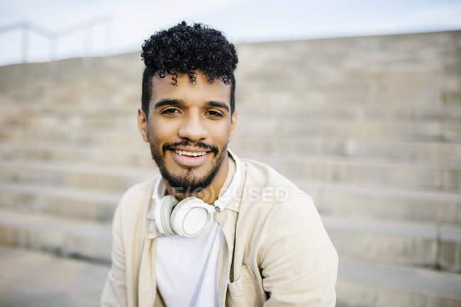 Jeune homme souriant aux cheveux bouclés noirs portant un casque sans fil — Photo de stock