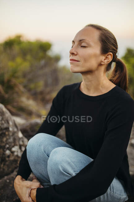 Femme avec les yeux fermés assis sur le rocher — Photo de stock