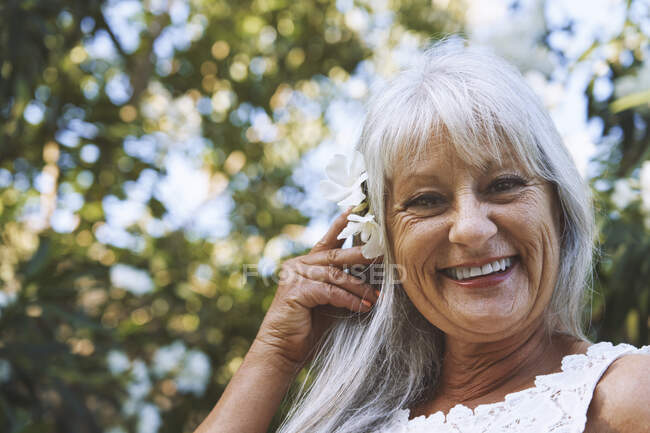 Sorridente donna anziana che indossa fiori nei capelli al parco — Foto stock