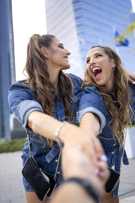 Cheerful twin sisters holding hand of female friend — Stock Photo