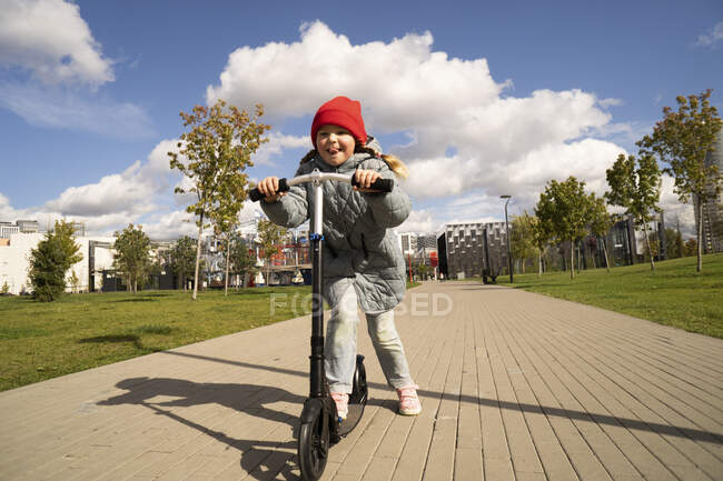 Дівчинка їде на іграшковому скутері на стежці в парку в сонячний день. — стокове фото