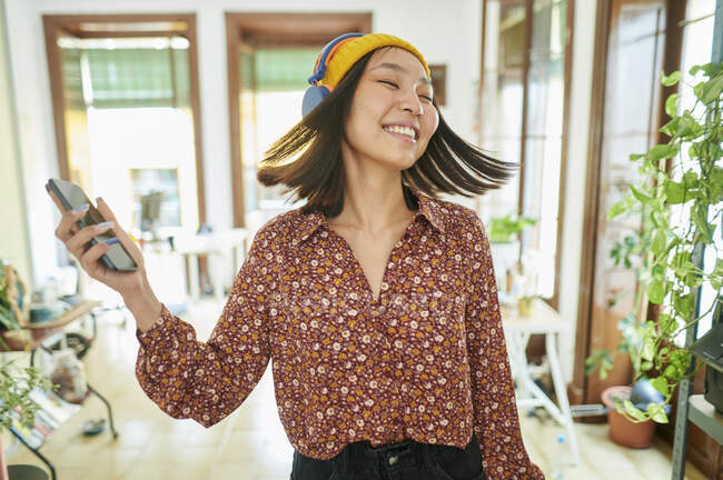 Lächelnde Geschäftsfrau wirft Haare, während sie im Büro über Kopfhörer Musik hört — Stockfoto