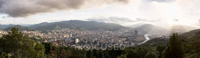 España, Vizcaya, Bilbao, Panorama de la ciudad al atardecer con montañas de fondo - foto de stock