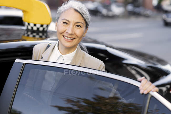 Усміхнена жінка відчуває, як сіре волосся входить в таксі — стокове фото