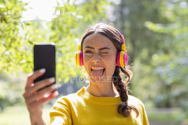 Woman Sticking Out Tongue While Taking Selfie Through Smart Phone At Park — Young Women Adults 