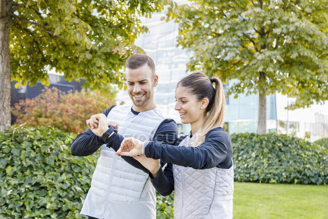 Улыбающиеся мужчина и женщина проверяют наручные часы в парке — стоковое фото