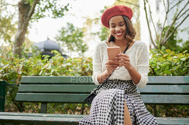 Усміхнена жінка користується мобільним телефоном у парку. — стокове фото