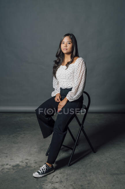 Hermosa mujer seria sentada en silla delante de fondo gris - foto de stock