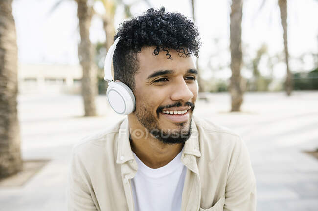 Sorrindo jovem ouvindo música através de fones de ouvido sem fio — Fotografia de Stock