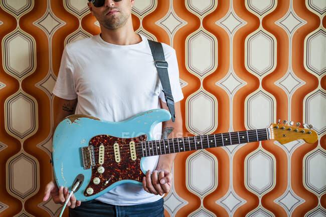 Junger männlicher Musiker hält Gitarre vor Wand — Stockfoto