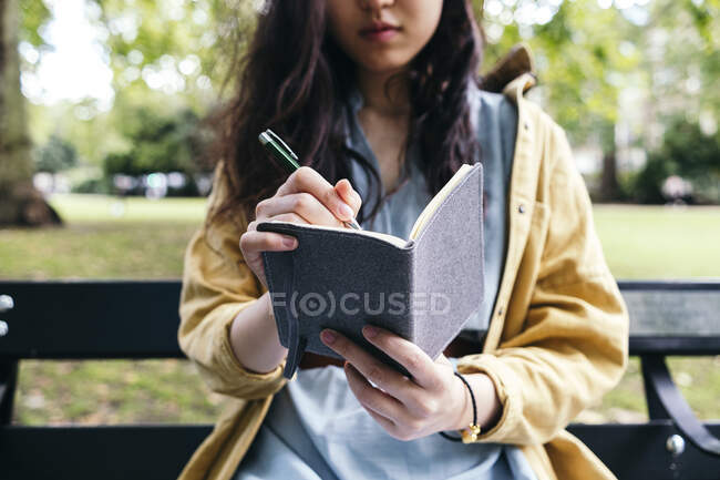 Mujer joven escribiendo en el diario en el parque - foto de stock
