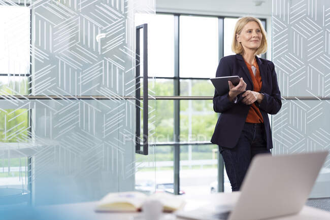 Mature female professional with blond hair holding digital tablet in office — Stock Photo