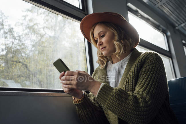 Mitte erwachsene Frau benutzt Smartphone, während sie im Zug sitzt — Stockfoto