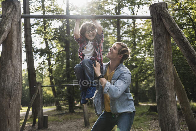 Padre aiutare figlio appeso su attrezzature da gioco nel parco — Foto stock