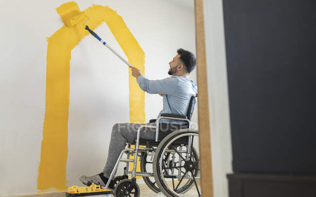 Homme avec handicap mur de peinture à travers rouleau de peinture à la maison — Photo de stock