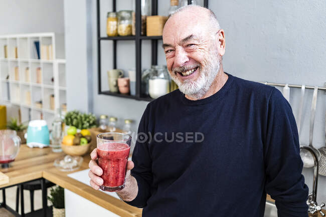 Happy senior man holding smoothie glass at home — Stock Photo