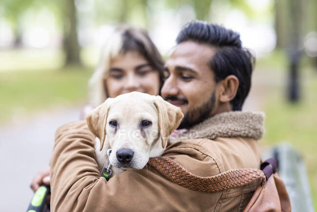 Jovem sorridente carregando cachorro no parque público — Fotografia de Stock