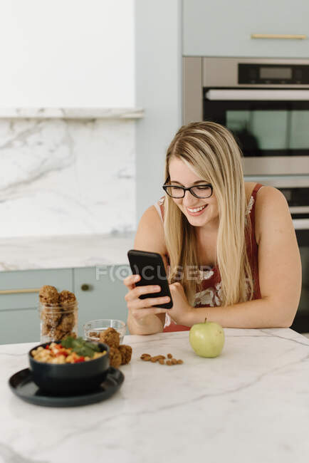 Female nutrient expert photographing food through mobile phone in kitchen — Stock Photo