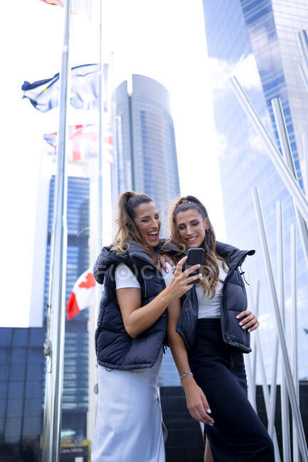 Happy twin sisters sharing smart phone in city — Stock Photo