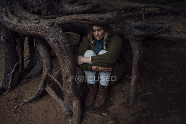 Verlorene Frau sitzt unter Baumwurzeln und umarmt Knie — Stockfoto