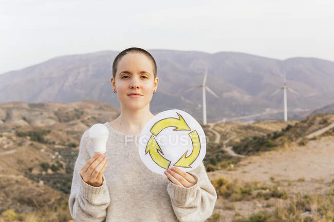 Mulher segurando lâmpada e símbolo de reciclagem desenho no parque eólico — Fotografia de Stock