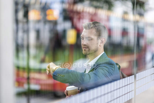 Young businessman checking time on wristwatch seen through glass — Stock Photo