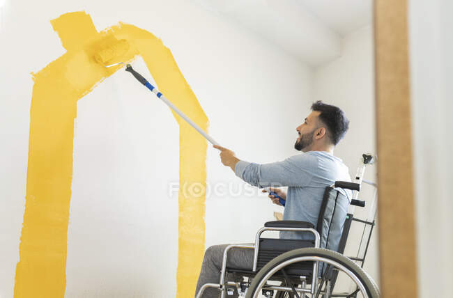 Uomo seduto su sedia a rotelle pittura parete in soggiorno — Foto stock