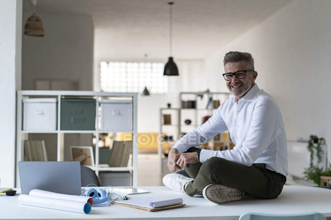 Smiling businessman sitting cross-legged on desk — Stock Photo