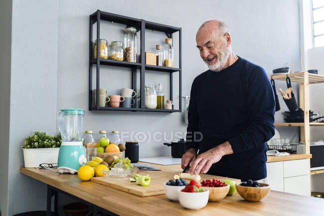 Uomo anziano taglio banana sul tagliere in cucina — Foto stock