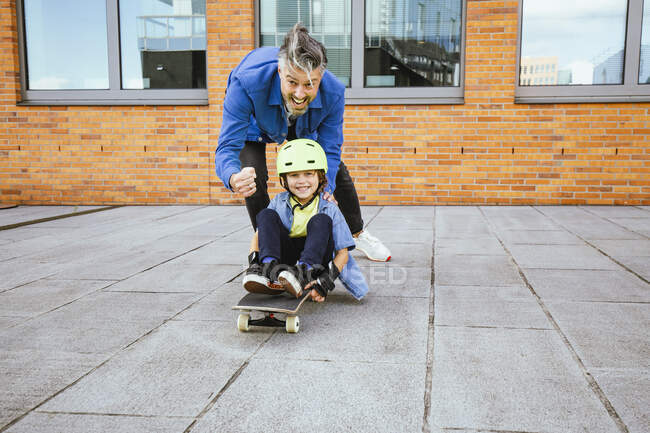 Playful father and son playing with skateboard on footpath — Stock Photo