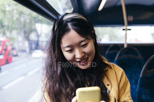 Mujer sonriente usando el teléfono inteligente en el autobús - foto de stock