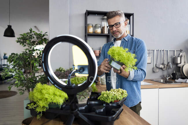Man holding potted plant while vlogging through smart phone in kitchen — Stock Photo